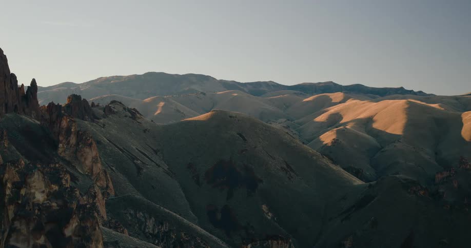 View of a mountain and canyon landscape at sunrise with golden sunlight casting warm hues over the rugged terrain