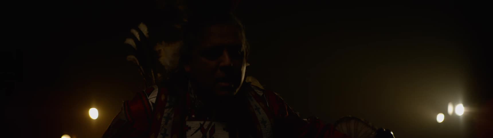 The man in a tribal costume is dancing in the dark