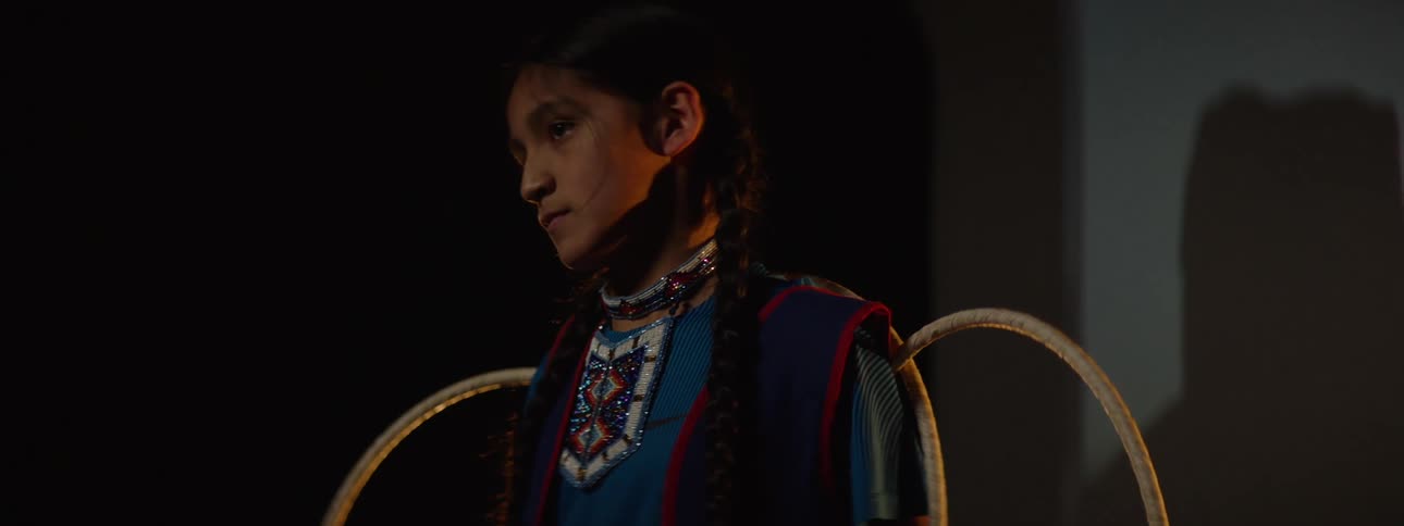 Girl with braids and colorful beaded necklace wears traditional costume while holding circular hoops