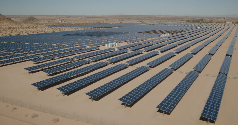 A wide solar farm stretches across a desert landscape under clear skies