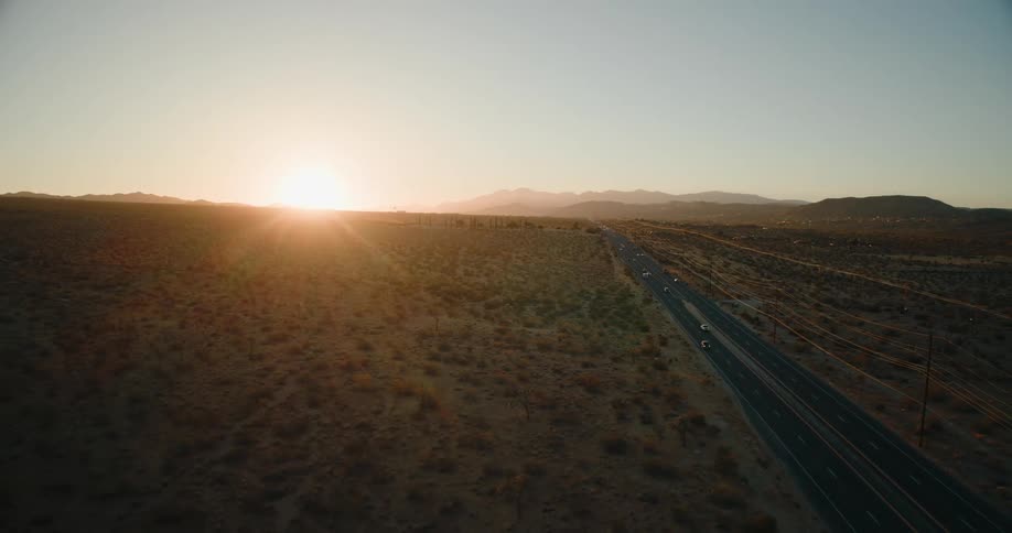 A long desert highway stretches into the horizon as the sun sets behind distant mountains