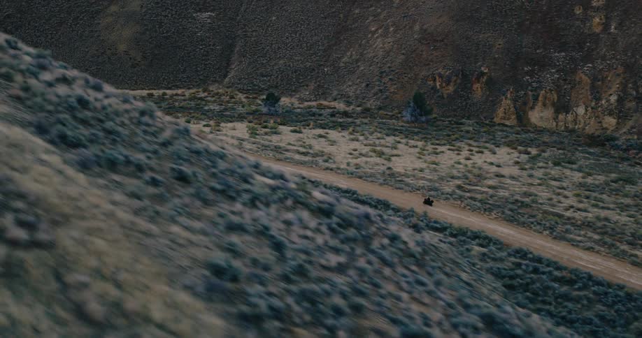 A man on a motorcycle riding on a dirt road surrounded by mountains