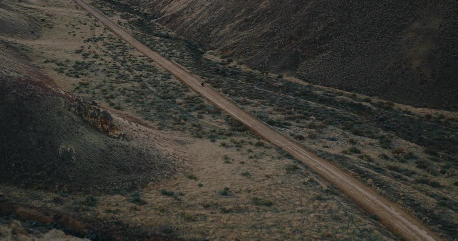 Aerial view of a person riding a motorcycle on a dirt road surrounded by a mountain valley