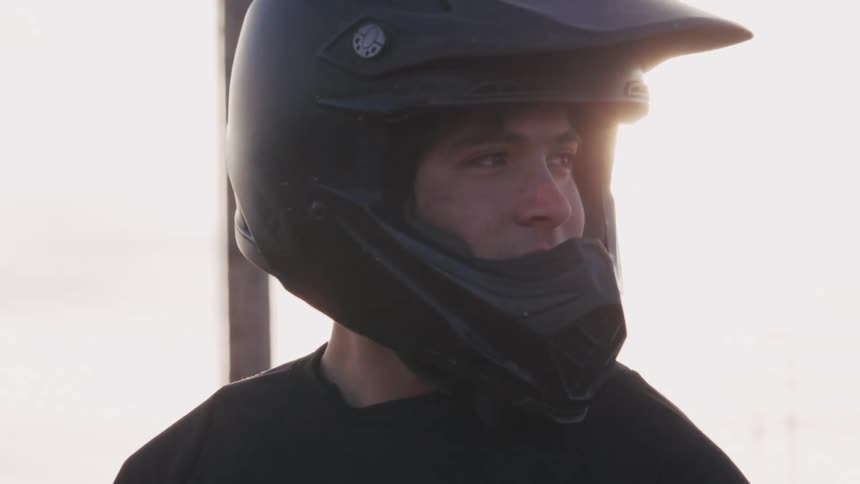 A motorcycle racer wearing a helmet glances left and right under the bright midday sun