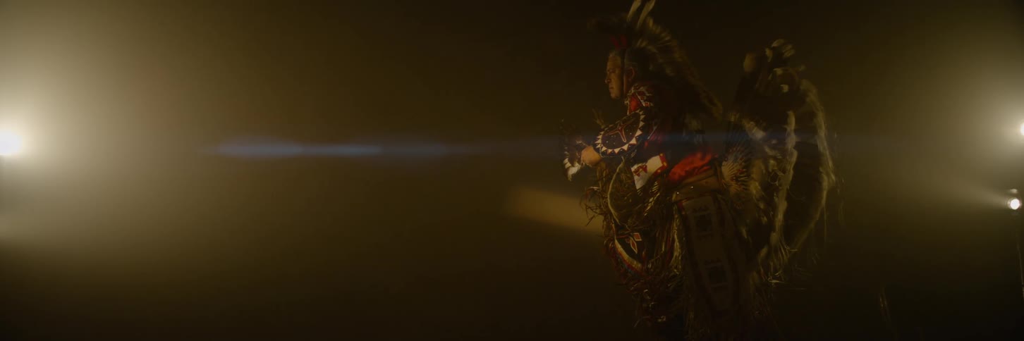 Person in traditional indigenous clothing performing in a lowlit room