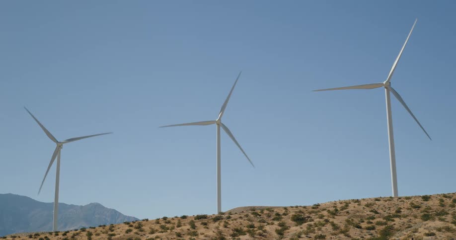 Three wind turbines rotate on a desert hill under clear blue sky