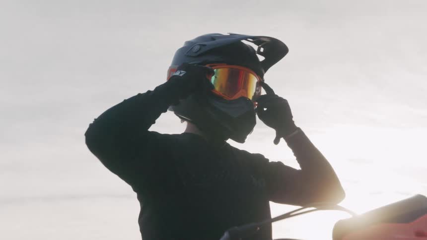 A man adjusts his helmet as he gets ready to ride his dirt bike