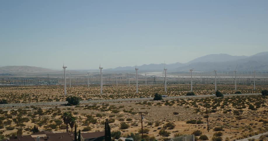 A wind farm stretches across a vast desert landscape under a clear sky
