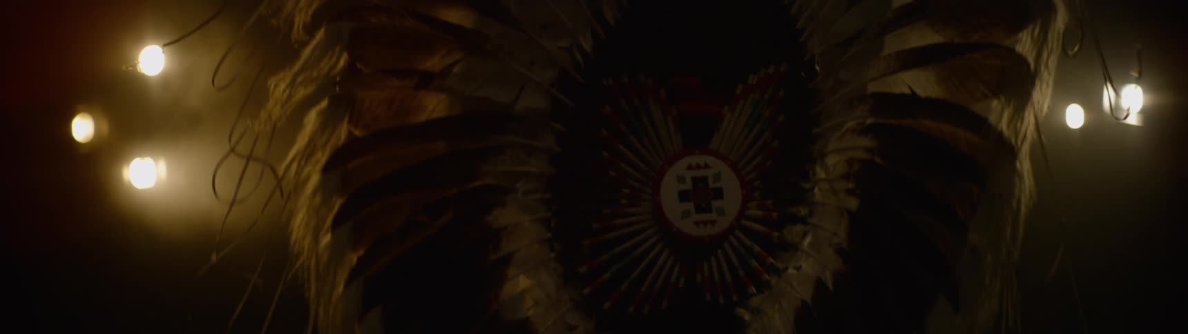 Native american wearing ceremonial attire dances under bright lights
