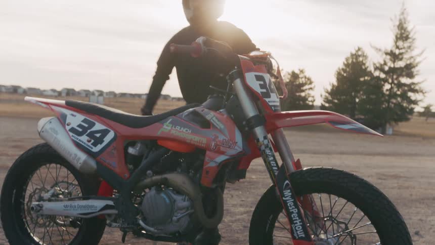 A dirt bike rider in full gear prepares to ride in an open outdoor area during sunset