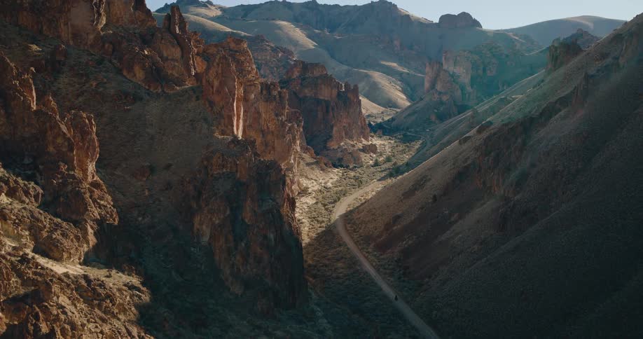 A winding dirt road cuts through a rugged canyon landscape surrounded by steep rocky cliffs
