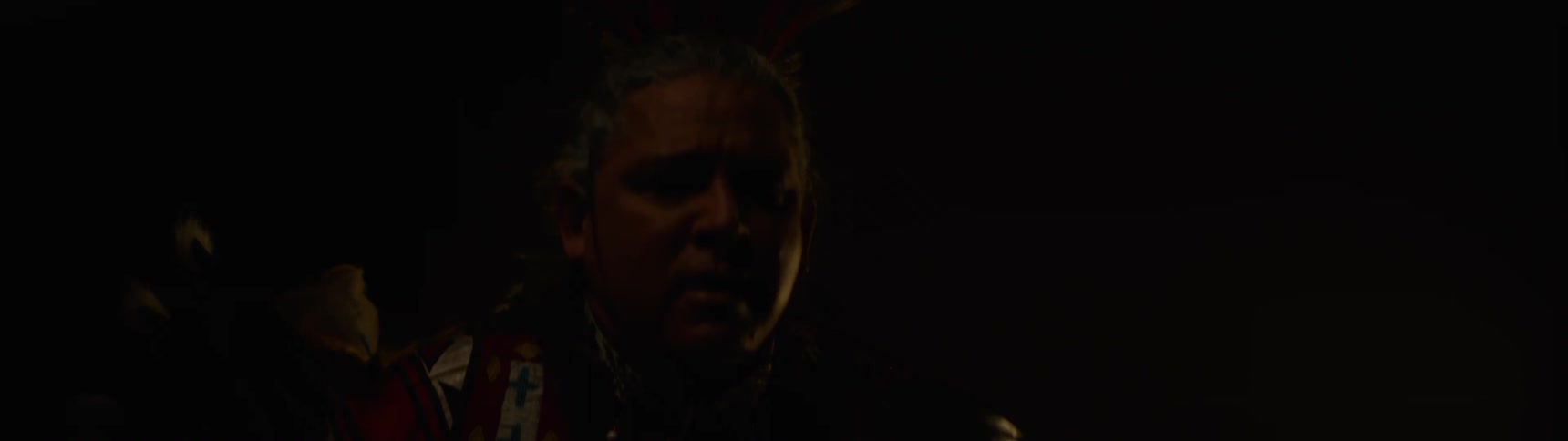 A close up of a native american man wearing a headdress in a dimly lit environment