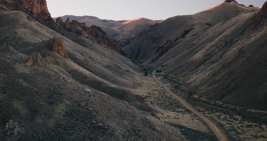 A winding dirt road cuts through a dry rugged canyon surrounded by steep rocky hills