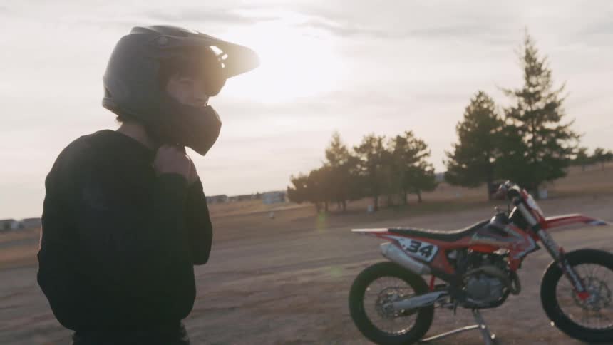 Man taking off a helmet next to a motorcycle outdoors