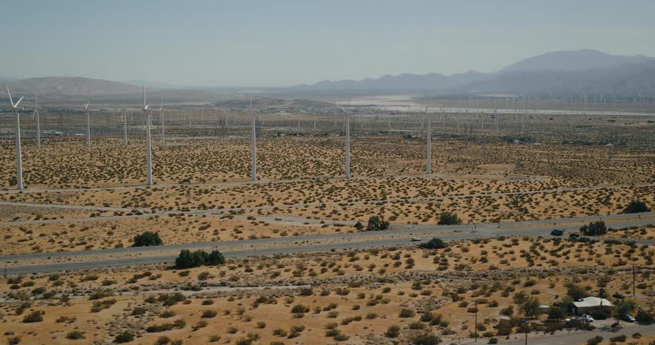 A wind turbine farm located beside a freeway under the bright midday sun