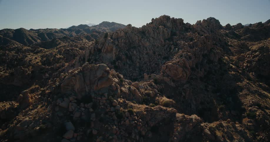 Jagged rock formations cover a sunlit rugged mountain range under a clear sky