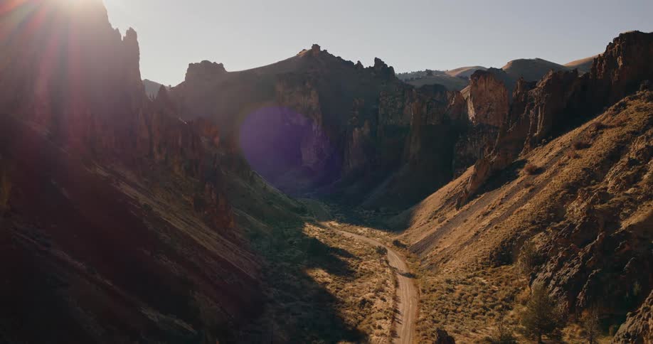 A dirt road winds through a sunlit canyon with steep rugged cliffs
