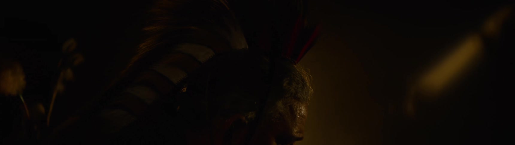 A native american man with feathers on his head lowering his head