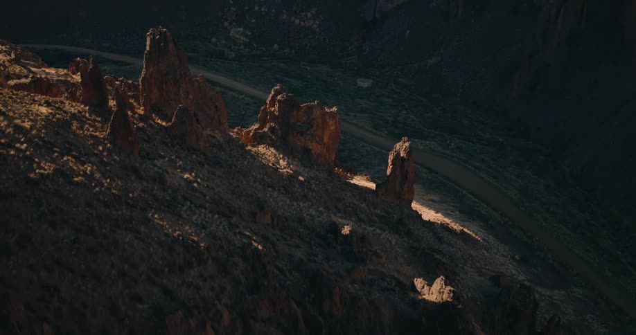 Sunlight hits jagged rock spires above a winding dirt road in a canyon