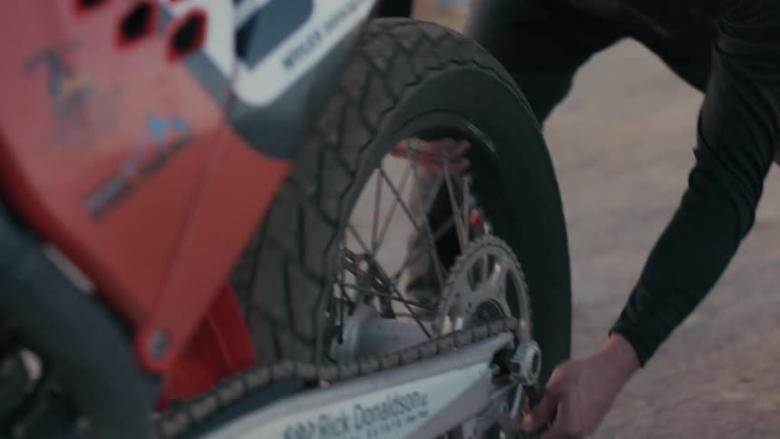 A closeup shot captures a persons hand adjusting the chain on the rear wheel of a motorcycle
