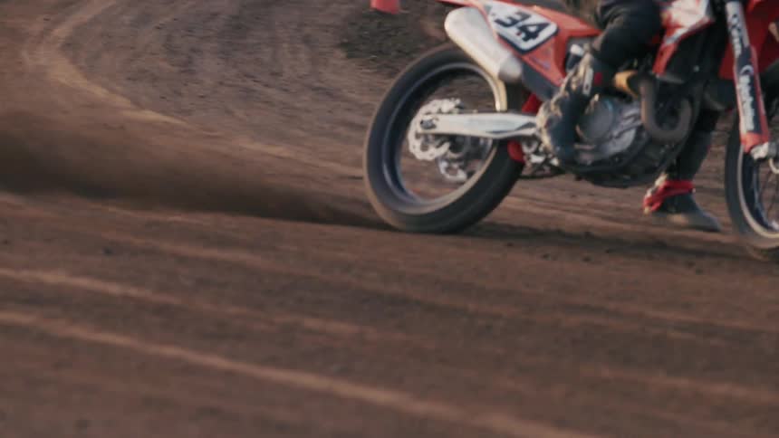 A motorcycle racer leans into a turn on a racetrack under the bright midday sun