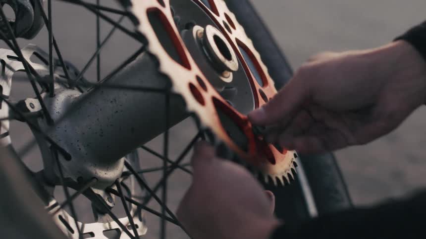 A person adjusts the rear gear mechanism of a motorbike wheel with their hands