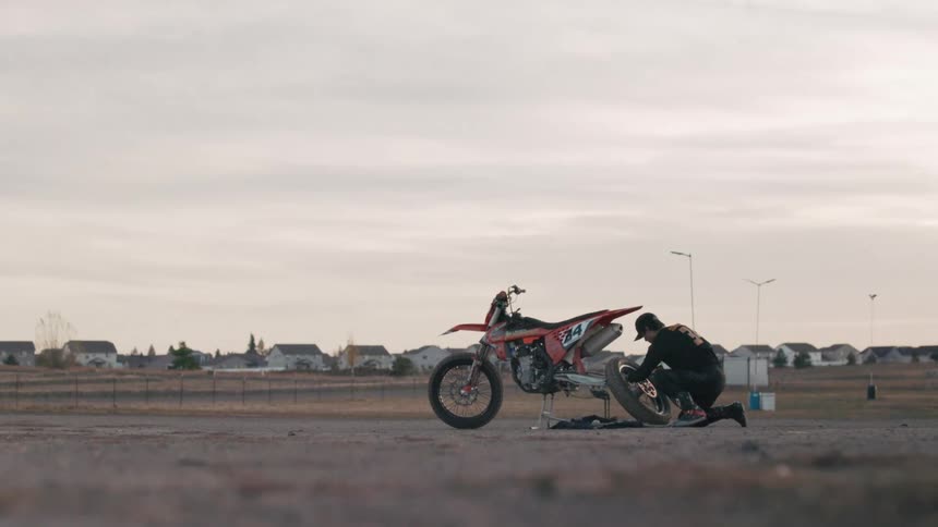A man is fixing the wheel on a dirt bike