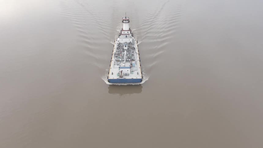 A cargo ship sails steadily down a wide muddy river viewed from above