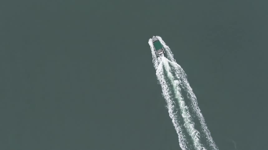 An overhead view captures a boat leaving a white wake as it travels across dark calm water