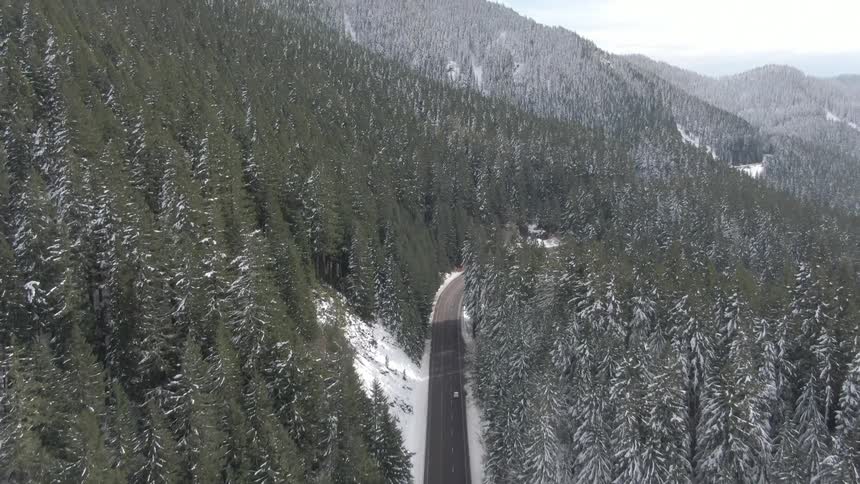A car on a road between forested mountains in winter