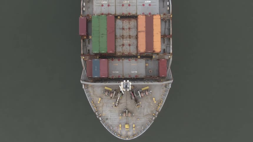 Aerial of a cargo ship carrying various shipping containers at sea during daytime