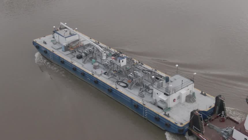 Tugboat pushes a large industrial barge across a muddy river