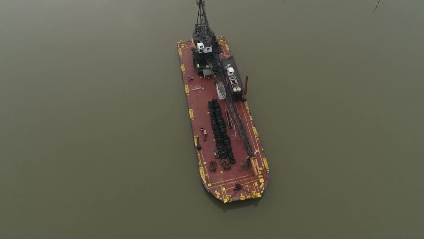 A large industrial barge floats in calm water near a dock area