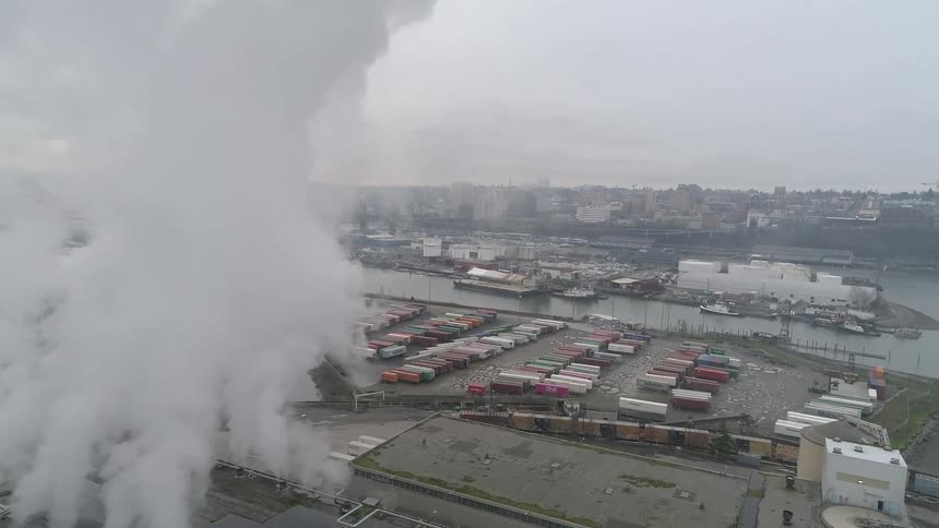 Smoke rises from the factory by the shipping containers
