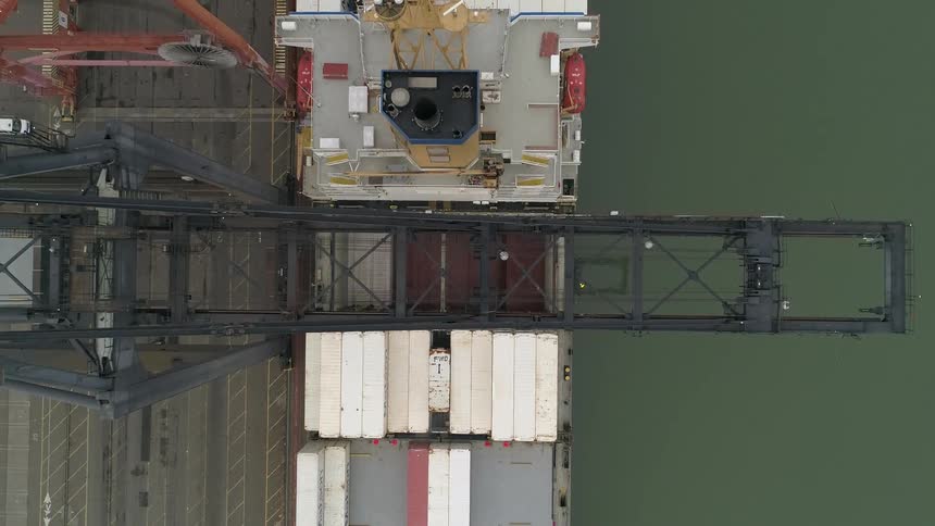 Aerial shot of a cargo ship being loaded at a dock by a large crane