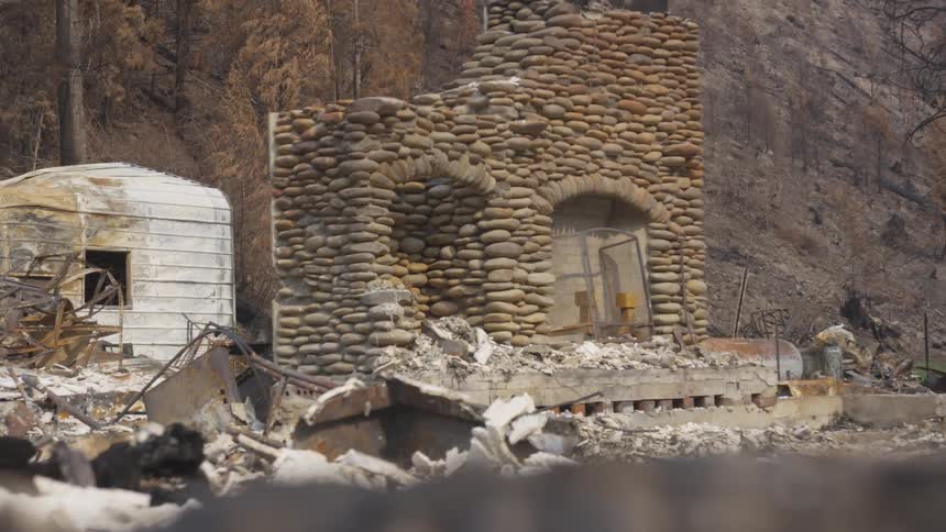 Stone structure stands amid debris in a forested area devastated by fire