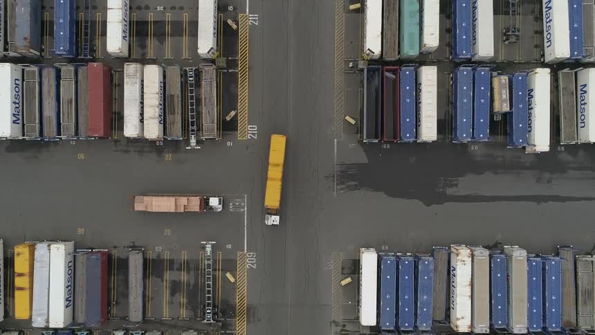 Aerial of trucks moving containers in a shipping container yard during the day