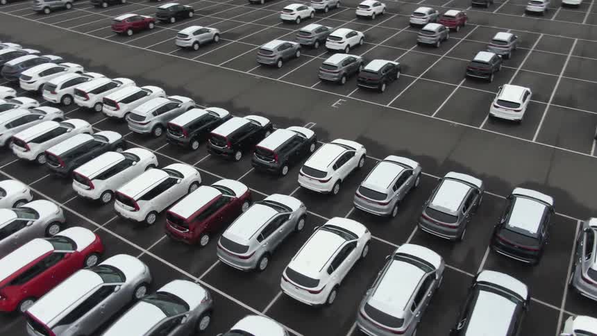An overhead view captures a large paved parking lot filled with numerous new white black and red cars arranged in neat rows