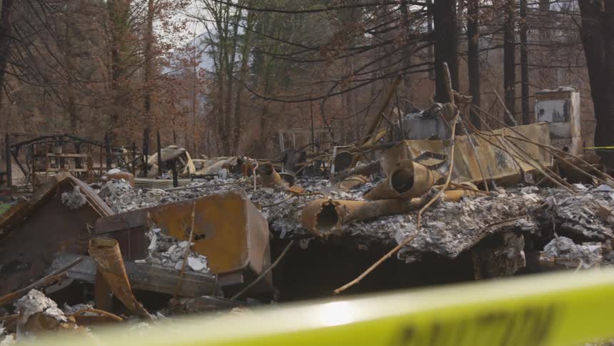 Caution tape dangles in front the ashy remnants of a burned down home in the forest