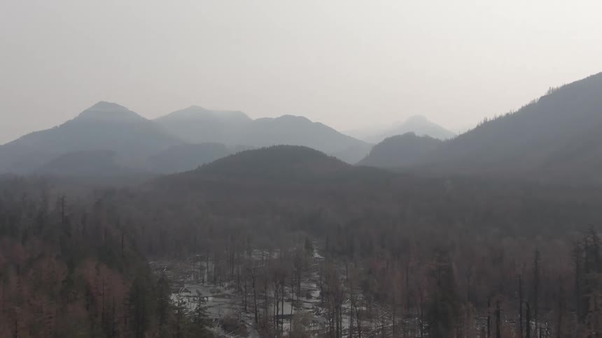 Aerial view of a misty mountain range above a forested valley with a river running through it