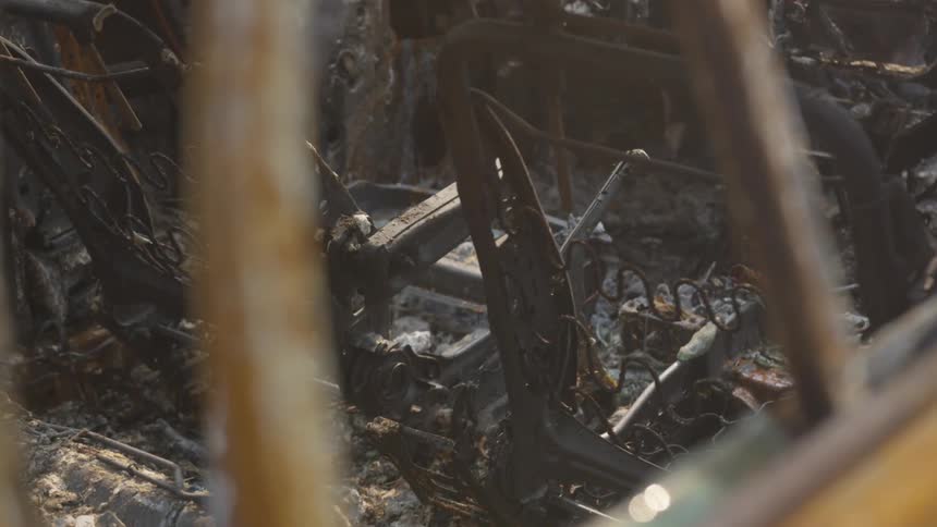 A panning shot reveals the charred interior of a destroyed vehicle focusing on the skeletal metal frames and springs of the burntout car seats