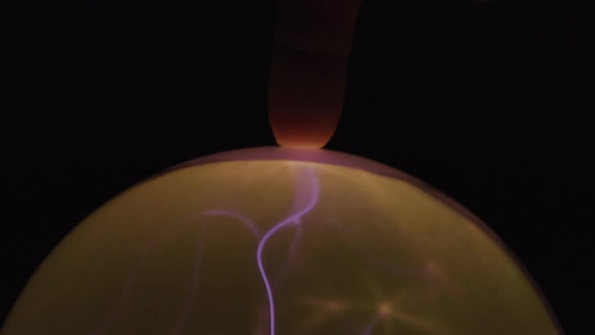 A single finger touches a plasma ball drawing a visible purple electrical current towards it against a dark background