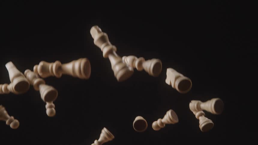 White wooden chess pieces being thrown up against a black background