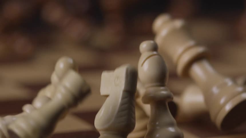 A chessboard jolted upward causing all the chess pieces to scatter and fall in different directions