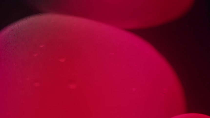 Pink globs of suspended gellike liquid move slowly inside a lava lamp