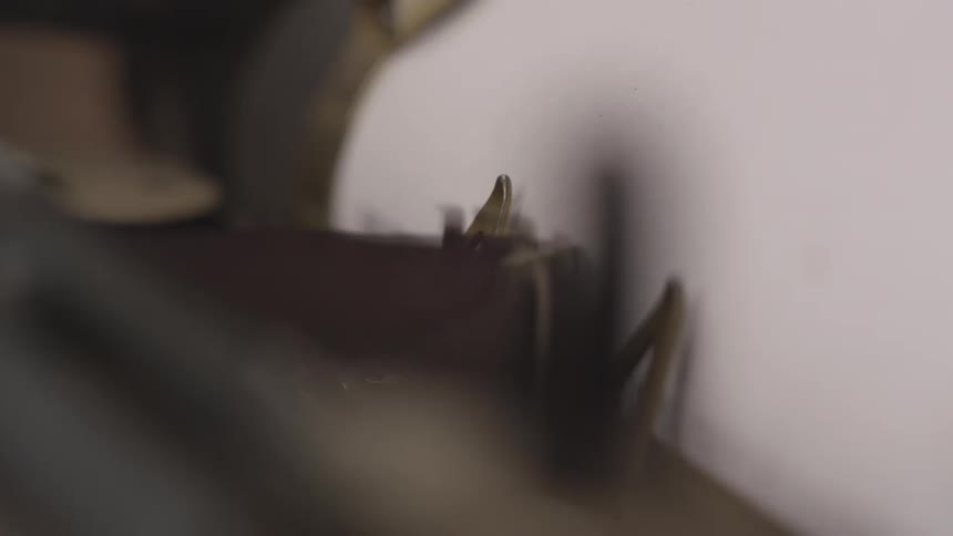 A closeup of a typewriter shows a typebars striking a sheet of paper
