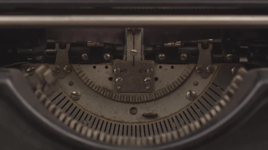 A closeup shows the typebar basket of a typewriter as two metal typebars strike the platen