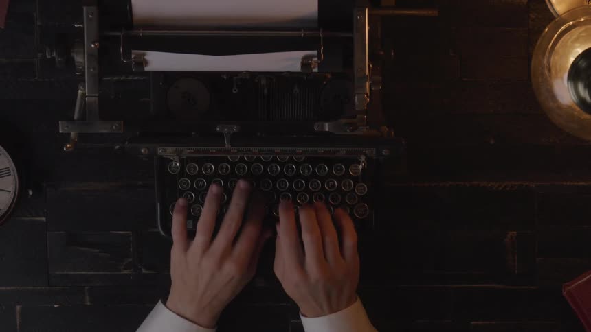 Hands typing on a vintage typewriter under warm lighting