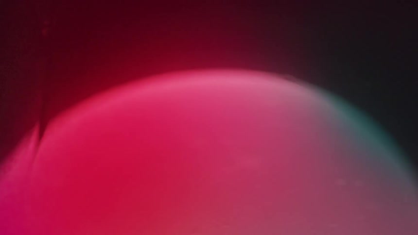 A blob with a gradient of red and green colors flows down a dark liquid