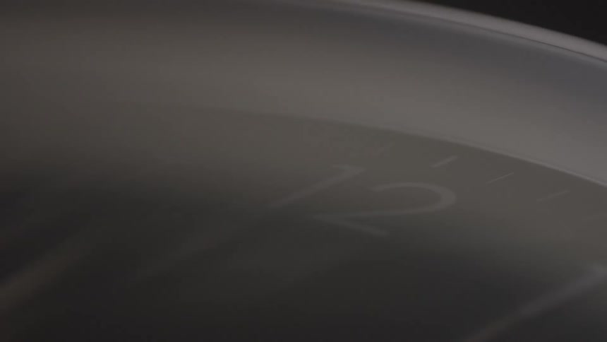 A closeup shot shows a dark clock face with only the numbers 11 and 12 visible and a white clock hand pointing towards the 12